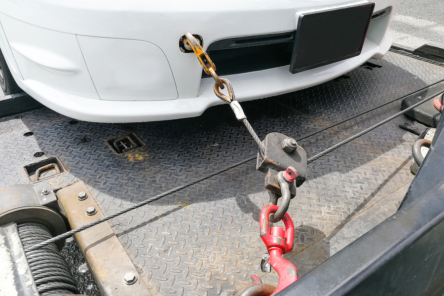 Broken down auto vehicle car towed onto flatbed tow truck with hook and chain